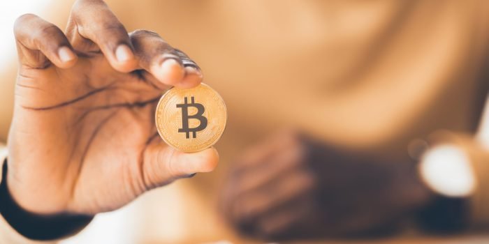 Digital Currency. African businessman holding golden bitcoin, close up of hand. Panorama, selective focus